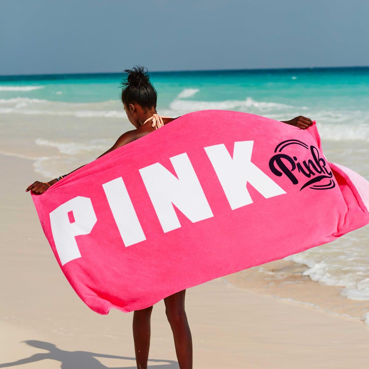 A woman at the beach holding a Victoria's Secret Pink Nation summer beach towel.