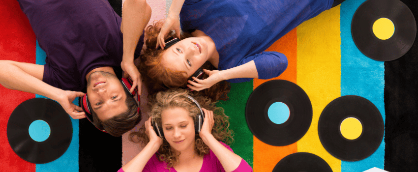 A group of young teachers relax on a vibrant rug, enjoying music together with devices purchased using electronics teacher discounts.