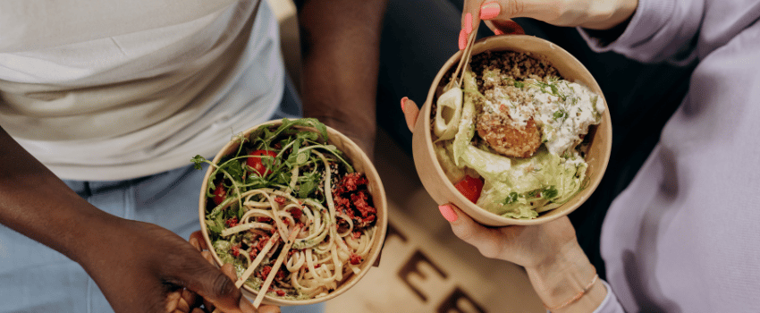 Two people with bowls of food and forks, highlighting a cooking class that offers food teacher discounts.