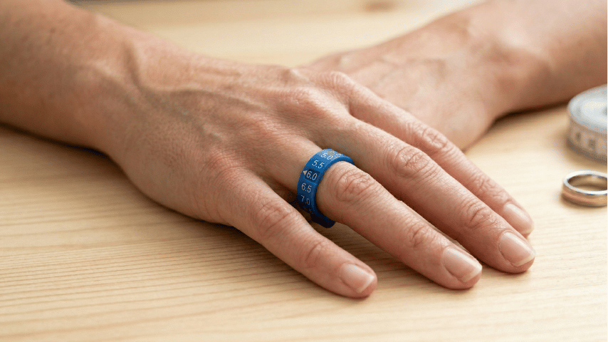 blue plastic ring sizer measuring a person's ring finger on a bright white desk background.