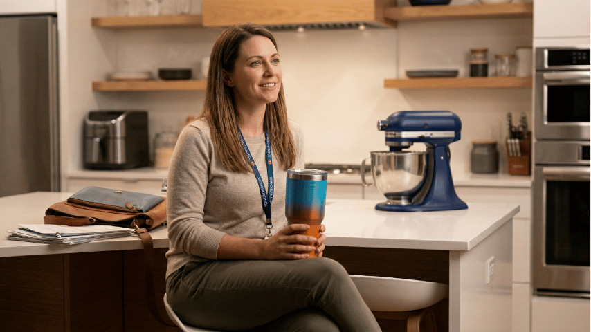 Teacher relaxing in a modern home kitchen holding an insulated travel tumbler next to a stand mixer.